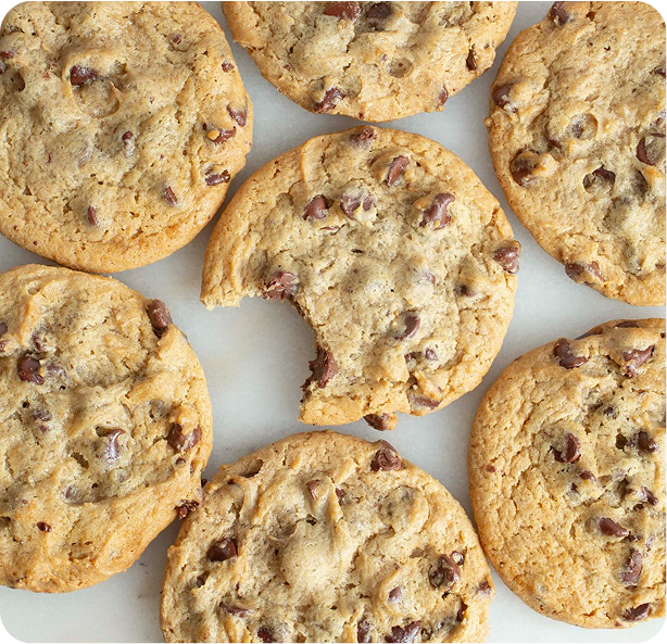 Golden brown chocolate chip cookies arranged on white background, showing chunky texture with dark chocolate chips and nuts scattered throughout