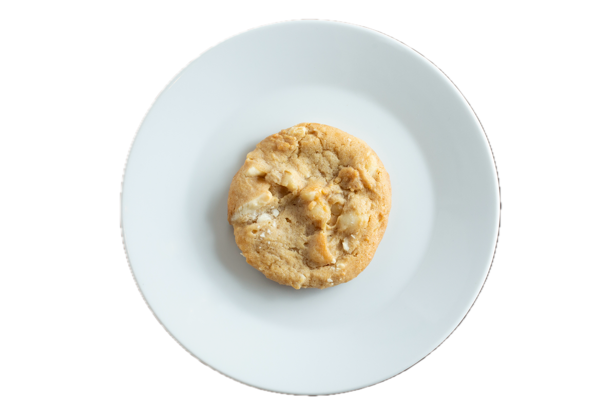 A golden-brown white chocolate macadamia nut cookie sits centered on a white plate against a black background.