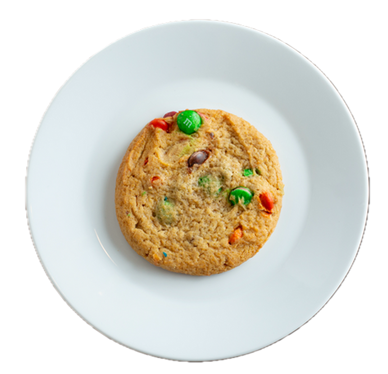 A golden-brown cookie with colorful M&M candies on a white ceramic plate against a white background.