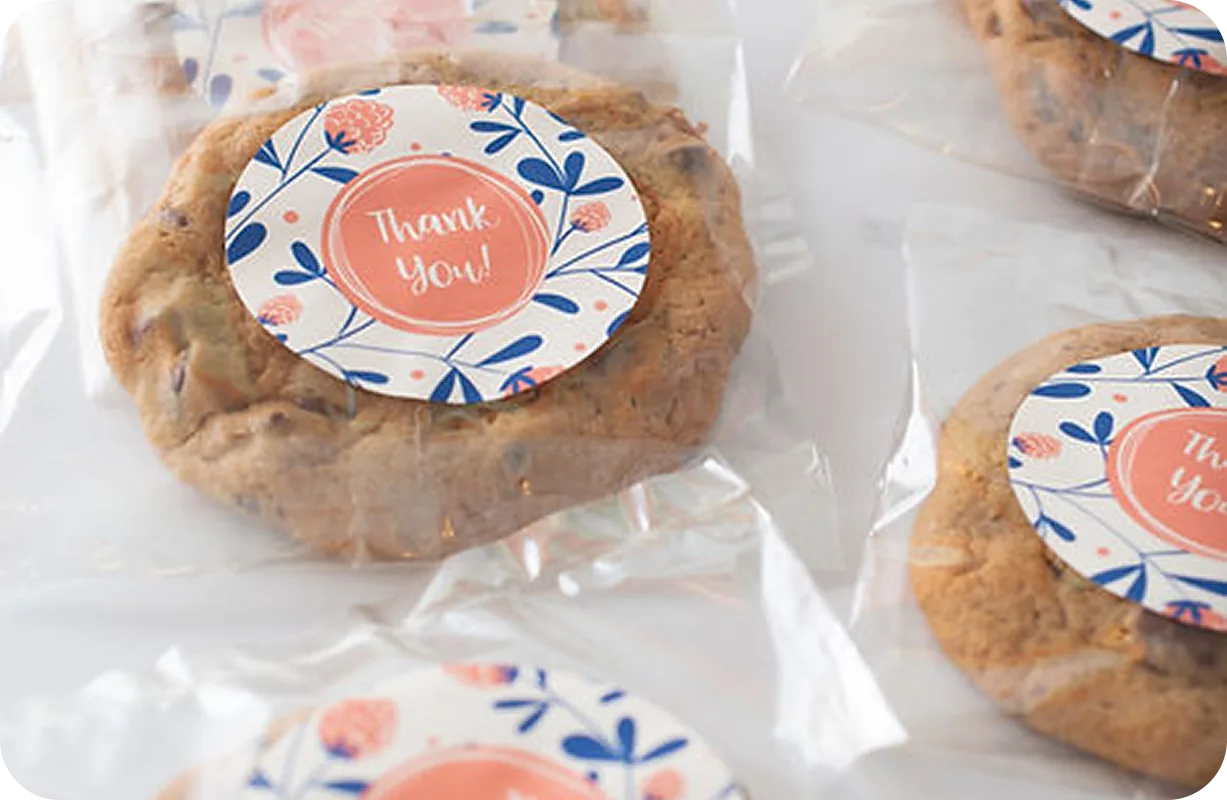 Chocolate chip cookies in clear plastic bags with circular "Thank You!" stickers featuring coral and blue floral design