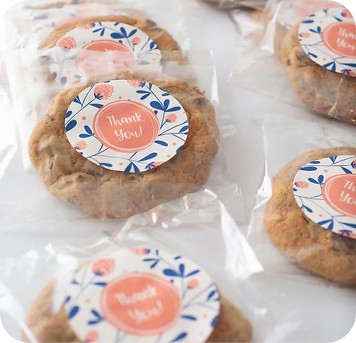 Individually wrapped cookies with circular "Thank You!" stickers featuring coral text and blue floral designs on clear plastic bags