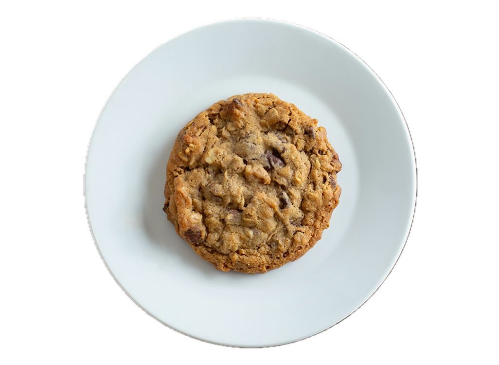 A golden-brown chocolate chip cookie with visible chocolate chunks and nuts on a white ceramic plate.