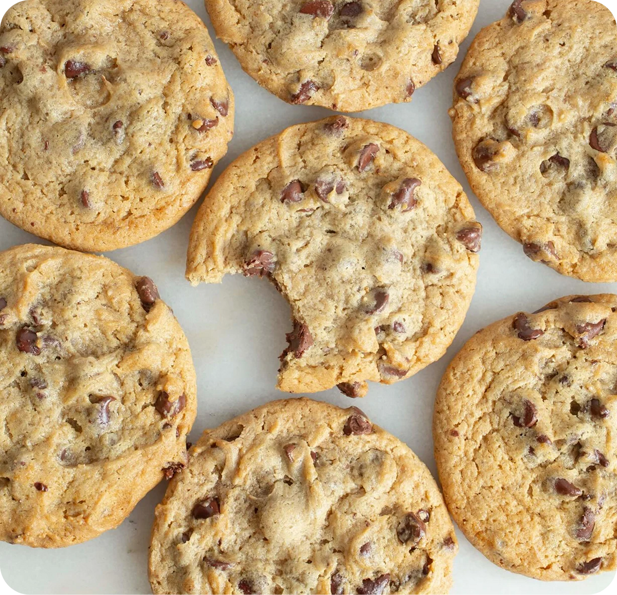 Golden brown chocolate chip cookies with visible chocolate chunks arranged on white parchment paper, shot from above