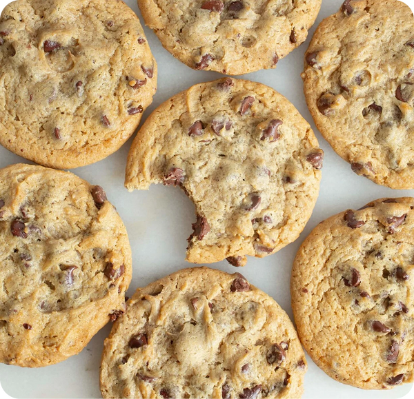 Golden brown chocolate chip cookies with visible chocolate chunks arranged on white parchment paper, shot from above