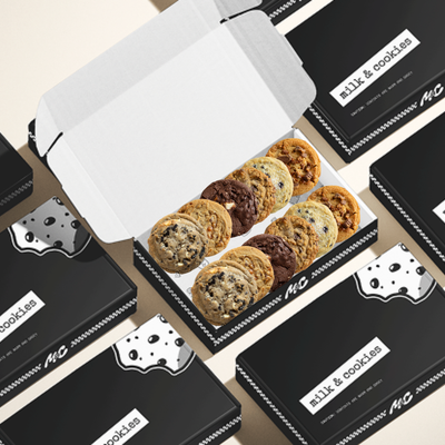 Assorted cookies in white box surrounded by black "milk & cookies" branded packages on beige background