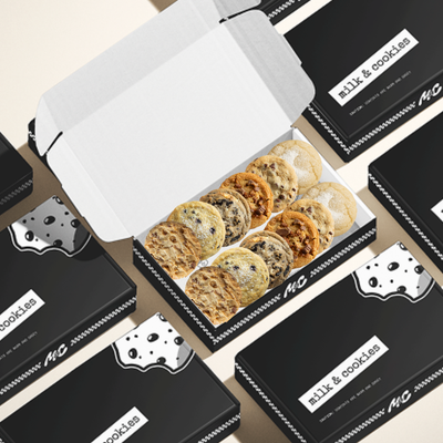 Box of assorted cookies with "Milk & Cookies" branded packaging scattered around on beige background