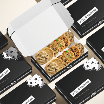 Box of assorted cookies with chocolate chips and colorful candies surrounded by black branded packaging boxes