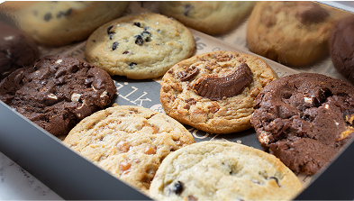 Assorted cookies in a baking pan including chocolate chip, double chocolate, and other varieties with golden and brown colors
