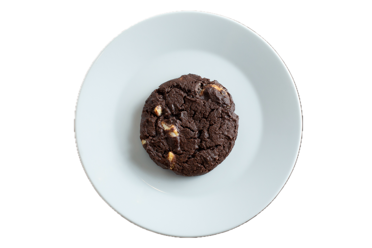 Dark chocolate cookie with white chocolate chunks on a white plate against black background