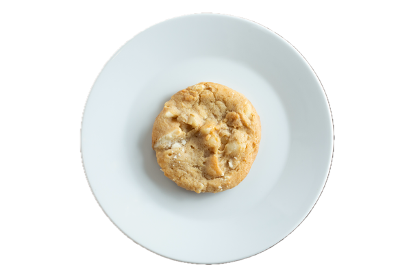A golden-brown white chocolate macadamia nut cookie sits centered on a white plate against a black background.