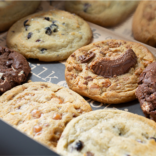 Assorted jumbo cookies in box including chocolate chip, blueberry, and caramel varieties on dark packaging